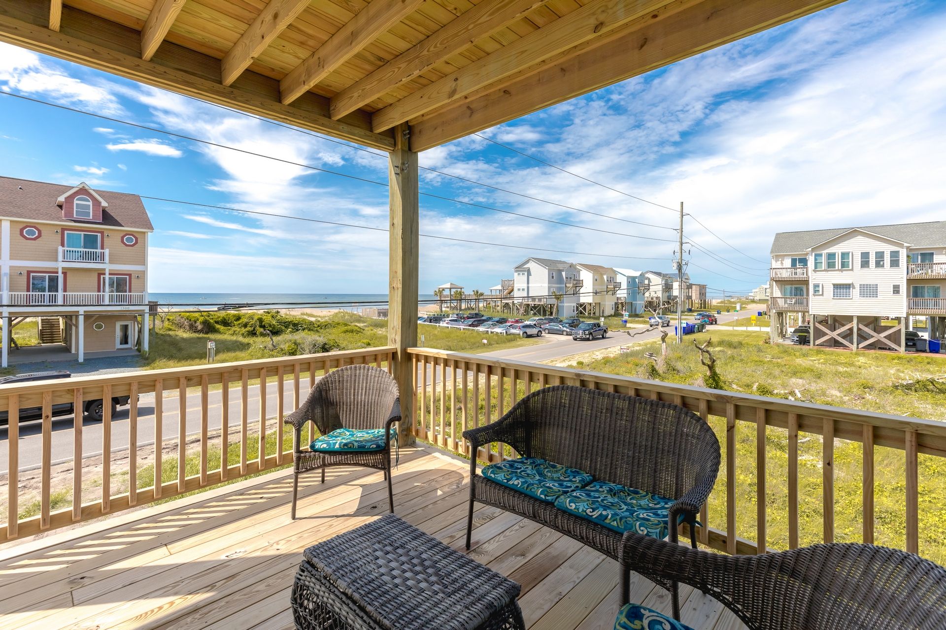 Une terrasse en bois, meublée de meubles en osier, qui offre une vue sur une plage et des immeubles résidentiels.