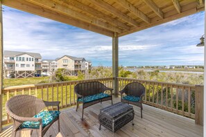 A wooden deck with wicker furniture and a view of residential buildings and water.