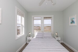 A bedroom with a large bed, two bedside tables, and a view of the outdoors through the windows.
