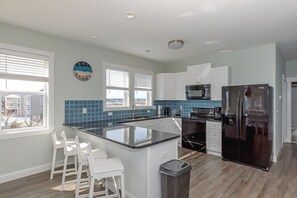 A modern kitchen with a central island, white cabinetry, a stainless steel refrigerator, and a view of the outside.