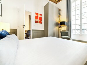 Une chambre d’hôtel avec un lit, un bureau, une chaise, une lampe et une fenêtre.