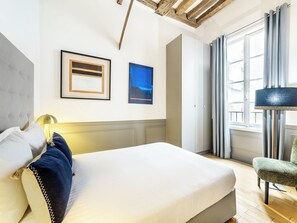 Una habitación de hotel con una cama, una silla, una lámpara y dos cuadros en la pared.