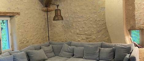 Una sala de estar acogedora con un amplio sofá seccional en forma de L, una mesa de centro de madera con revistas, vigas de madera a la vista y una pared de piedra.