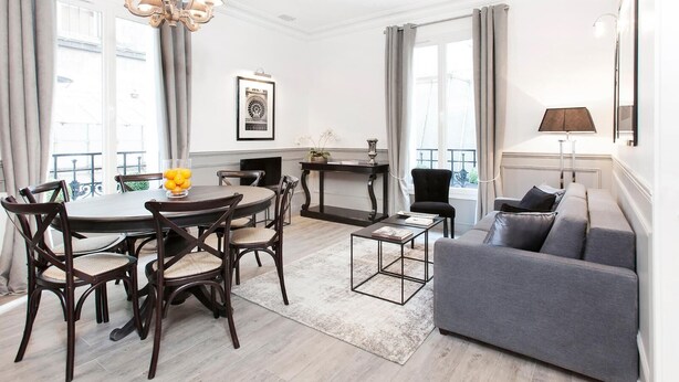 Ein modernes Wohnzimmer mit einem grauen Sofa, einem Esstisch mit Stühlen, einer Pendelleuchte und Blick ins Freie.