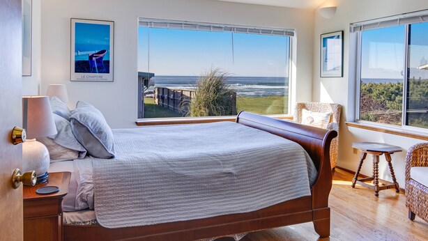 A bedroom with a large bed, a view of the sea, and a wooden floor.