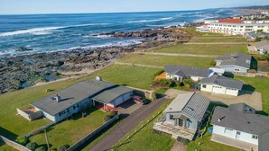 An aerial view of a coastal residential area with houses, a road, and a rocky shoreline.
