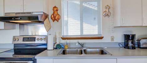 Une cuisine moderne équipée d’appareils électroménagers en acier inoxydable, d’un four encastré, d’un évier et d’une machine à café.