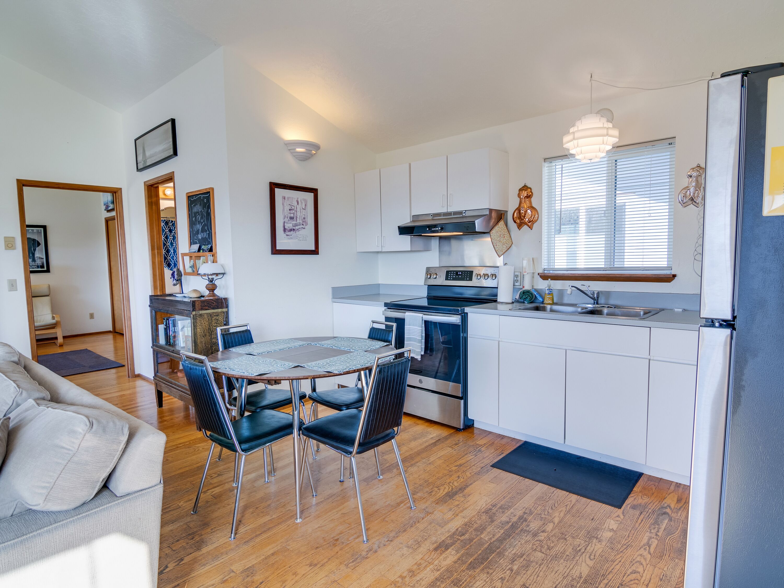 A modern kitchen with white cabinets, a stainless steel stove, and a dining area with a table and chairs.