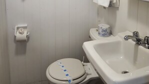 A bathroom with a toilet, sink, and a window above the sink. There are towels hanging on a rack and a toilet paper holder.