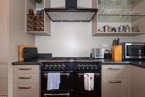 A kitchen with a stove, oven, and microwave. There are cabinets, a toaster, and a knife block.
