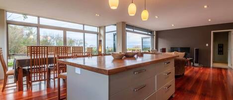 A modern kitchen with a large island, wooden dining table, and pendant lights.