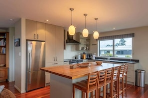 A modern kitchen with a central island, stainless steel appliances, pendant lighting, and a view through large windows. - Lake View Inn - Lake Views & Pet-Friendly (Rotorua)