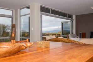 A modern dining area with a wooden table, a woven basket, and a view of the outdoors through large windows.