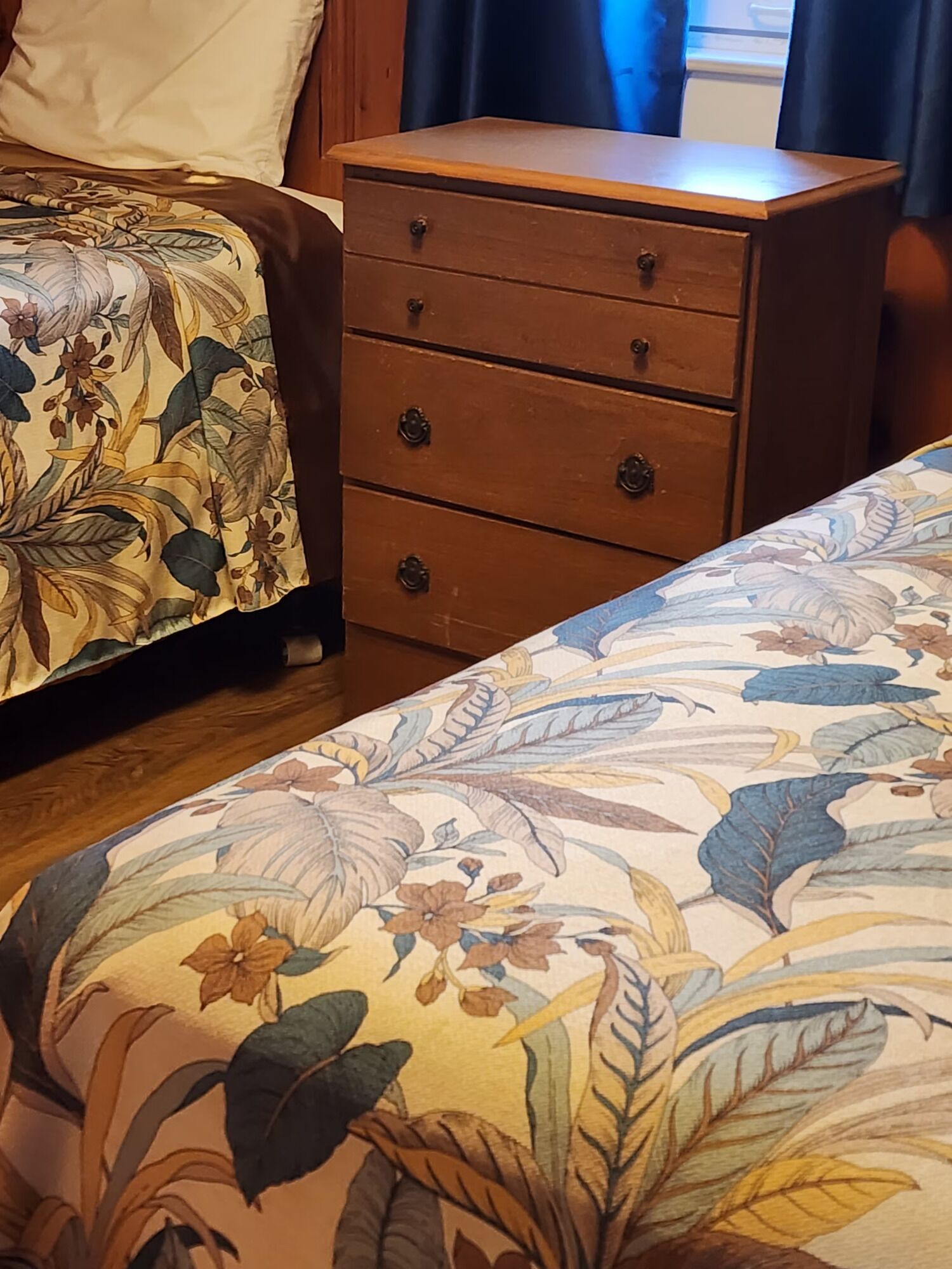 Una camera da letto con una coperta a fiori, un comò in legno con tre cassetti e un comodino.