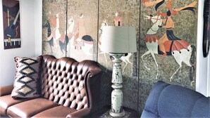 Ein Wohnzimmer mit einem braunen Ledersofa, einem blauen Sessel, einer weißen Lampe und einer Wand mit Wandgemälde.
