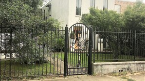 Ein von einer Mauer umgebenes Anwesen mit einem weißen Gebäude, einem Metallgitter und umgebender Bepflanzung.