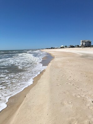 Une plage de sable avec des vagues, un ciel dégagé et des bâtiments en arrière-plan.