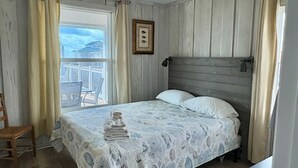 A bedroom with a bed, a window with curtains, a ceiling fan, and a view of the outside. - Great Getaway!! Relaxing Ocean Views (Saint George Island)