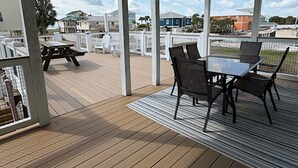 A covered outdoor area with a wooden deck, a picnic table, and a dining table with chairs. - Great Getaway!! Relaxing Ocean Views (Saint George Island)