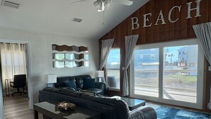 A modern living room with a sofa, a coffee table, and a view of the beach through large windows. - Great Getaway!! Relaxing Ocean Views (Saint George Island)