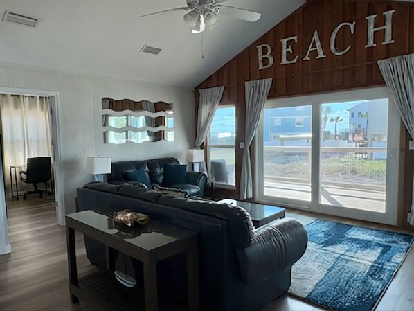 A modern living room with a sofa, a coffee table, and a view of the beach through large windows.