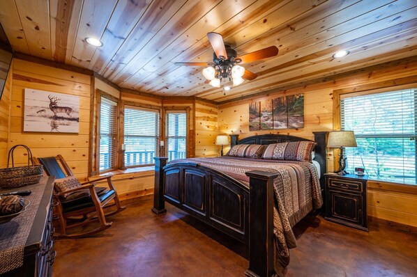 A wooden cabin bedroom with a bed, rocking chair, and a window with blinds.
