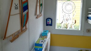 Een kamer met een bed, een raam met een dromenvanger, een surfboard en een klein plankje met dozen.