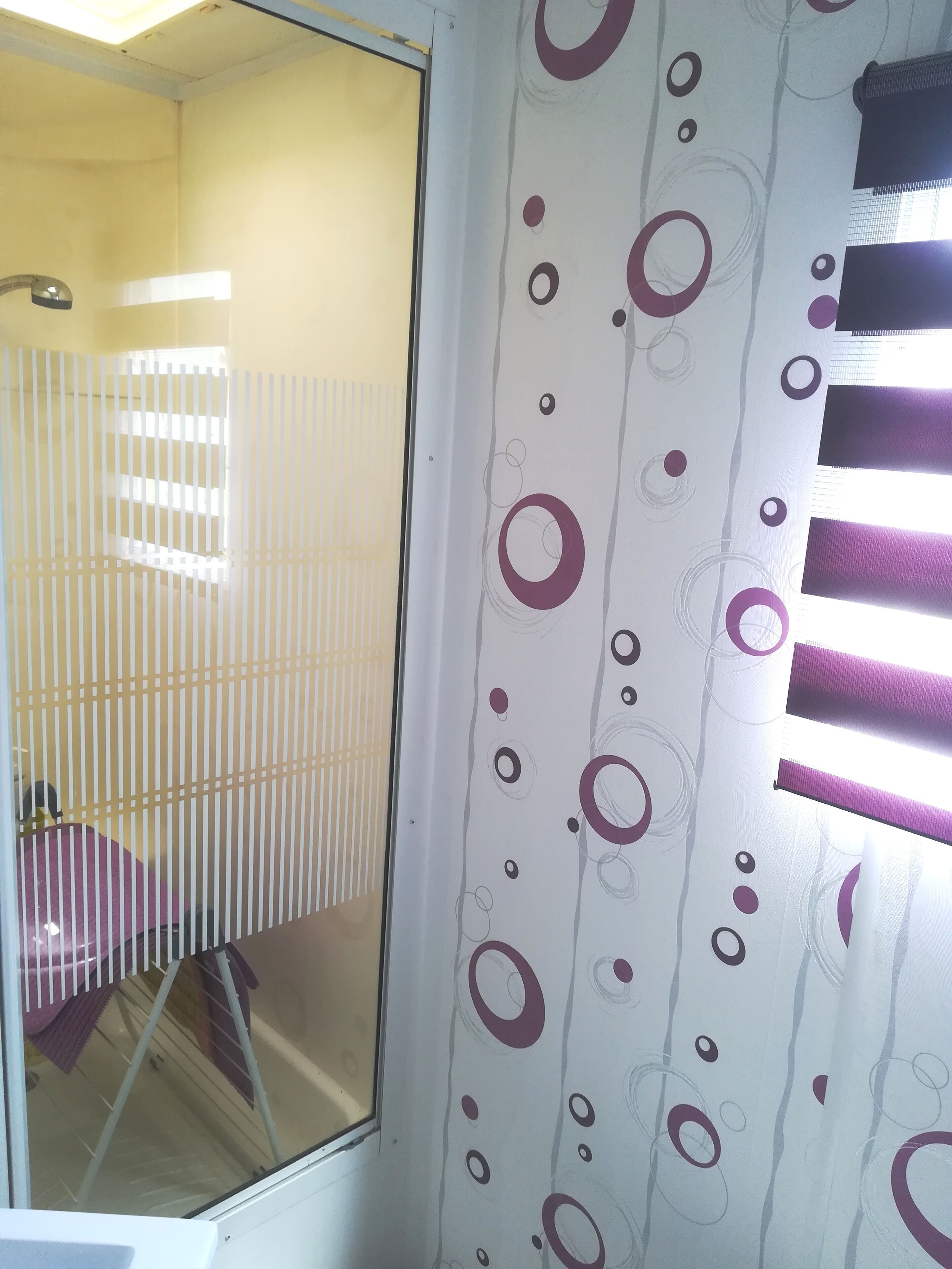 A room with a window, a curtain with a circular pattern, and a chair.