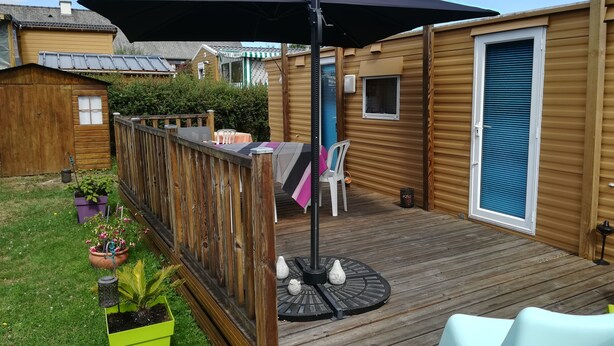 Een houten terras met een tafel en stoelen, omringd door een houten omheining en potplanten.