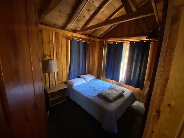 A wooden cabin bedroom with a bed, a nightstand, and a lamp.