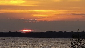 A sunset over a body of water with a silhouette of a tree line in the distance. - (Cedar Cabin) Cozy 2 Bedroom Cottage - Waterfront - No Pets (East Tawas)