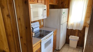 A compact kitchen with wooden cabinets, a white stove, a microwave, and a refrigerator. - (Cedar Cabin) Cozy 2 Bedroom Cottage - Waterfront - No Pets (East Tawas)