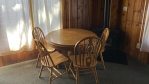 A wooden dining table with four chairs, a window with curtains, and a fireplace. - (Cedar Cabin) Cozy 2 Bedroom Cottage - Waterfront - No Pets (East Tawas)