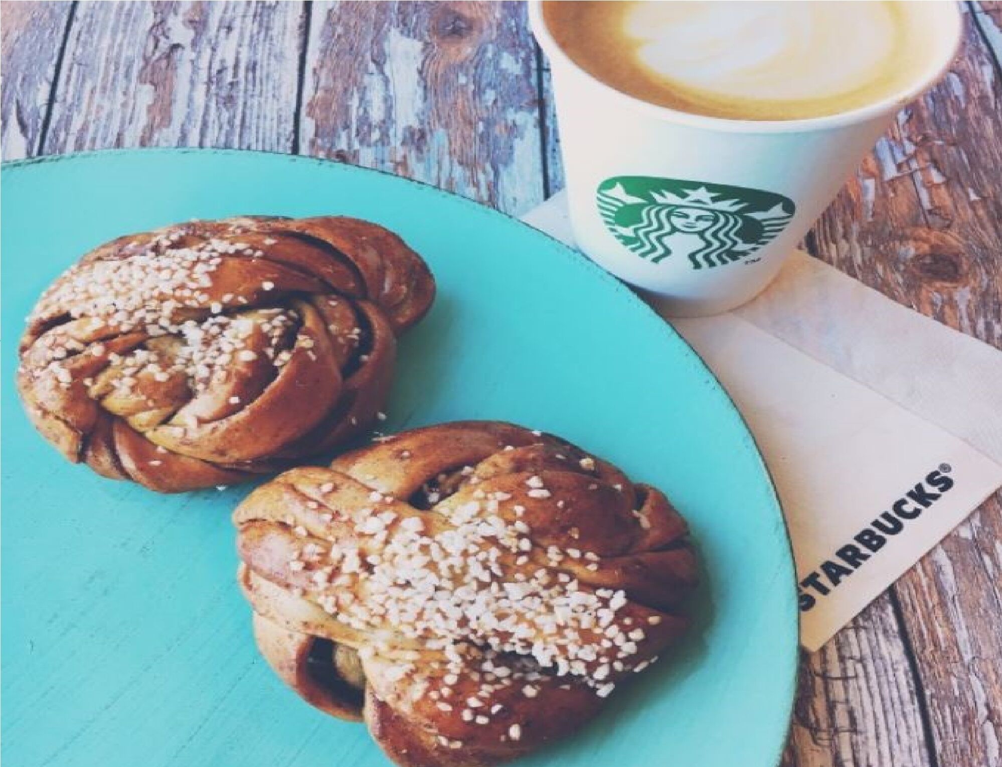 A plate with two cinnamon rolls and a Starbucks cup on a wooden table.