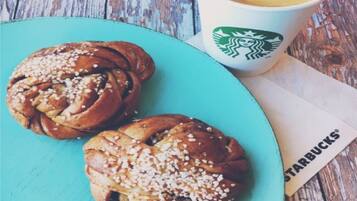 A plate with two cinnamon rolls and a Starbucks cup on a wooden table.