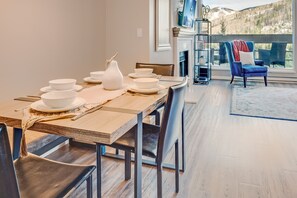 En matplats med ett träbord dukat för fyra personer, en vit vas och en öppen spis med utsikt över bergen.