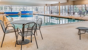 Un espace piscine intérieure comprenant une piscine, des chaises longues et des tables.