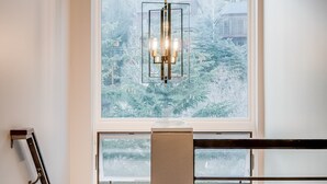 Un intérieur moderne avec un escalier, une grande fenêtre donnant sur un paysage enneigé et un luminaire suspendu.