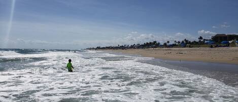 Una playa con olas, un niño en el agua y sombrillas de playa al fondo.