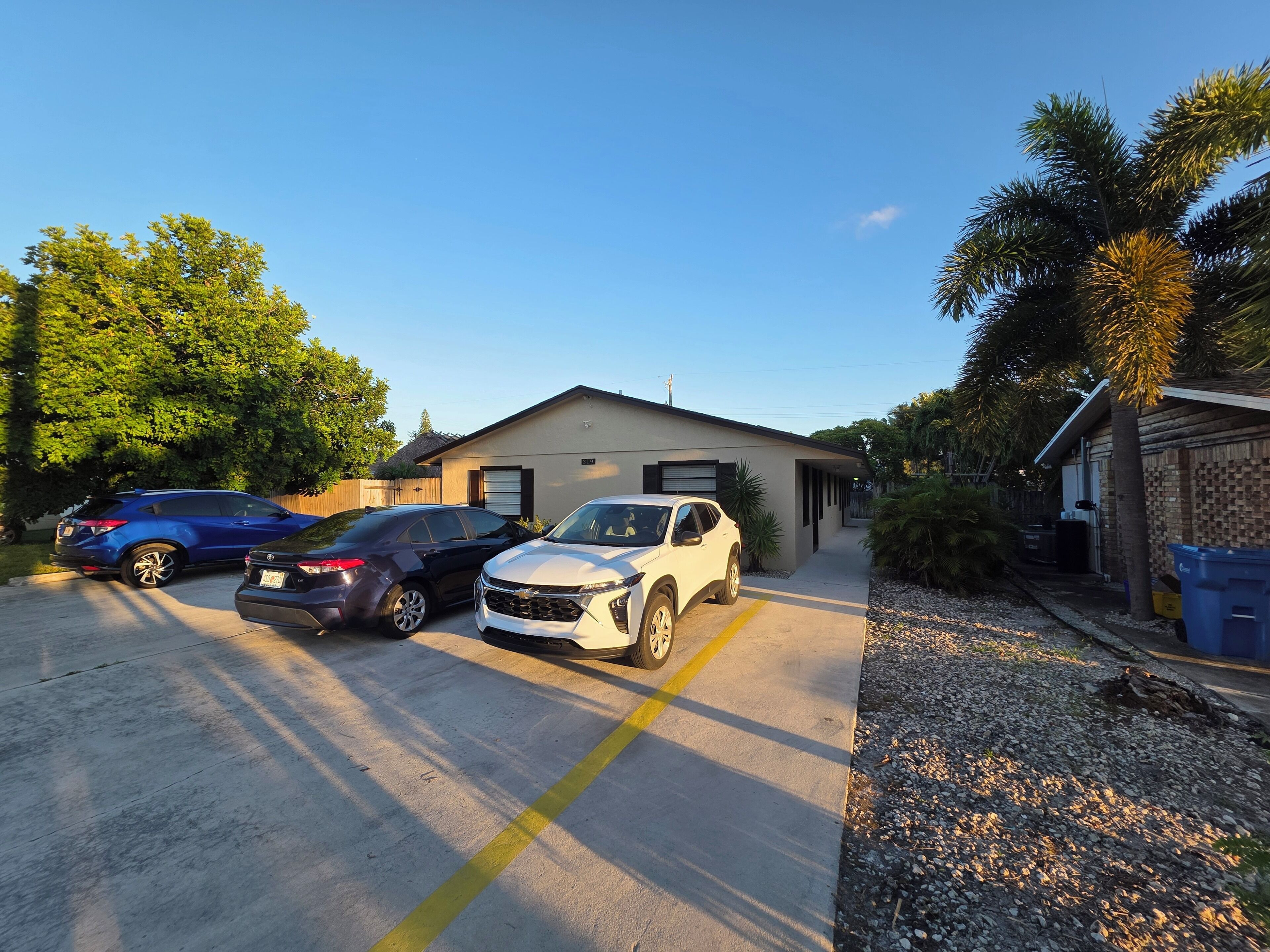 A residential driveway with three cars parked, a house with a garage, and a palm tree.