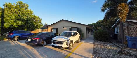 A residential driveway with three cars parked, a house with a garage, and a palm tree.
