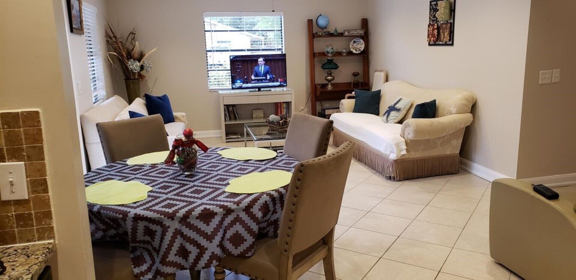 Un coin repas avec une table dressée pour quatre personnes, un canapé et un téléviseur en arrière-plan.