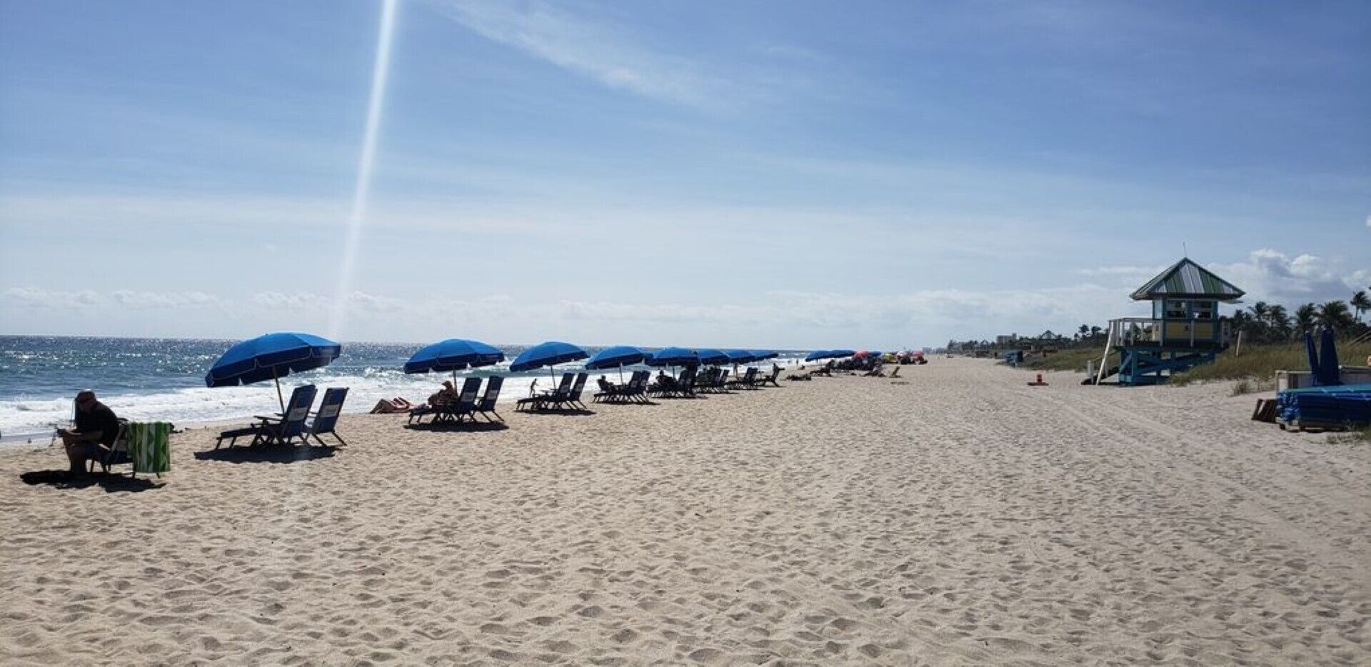 En strand med rader av solstolar och parasoller, ett livräddartorn och havet i bakgrunden.
