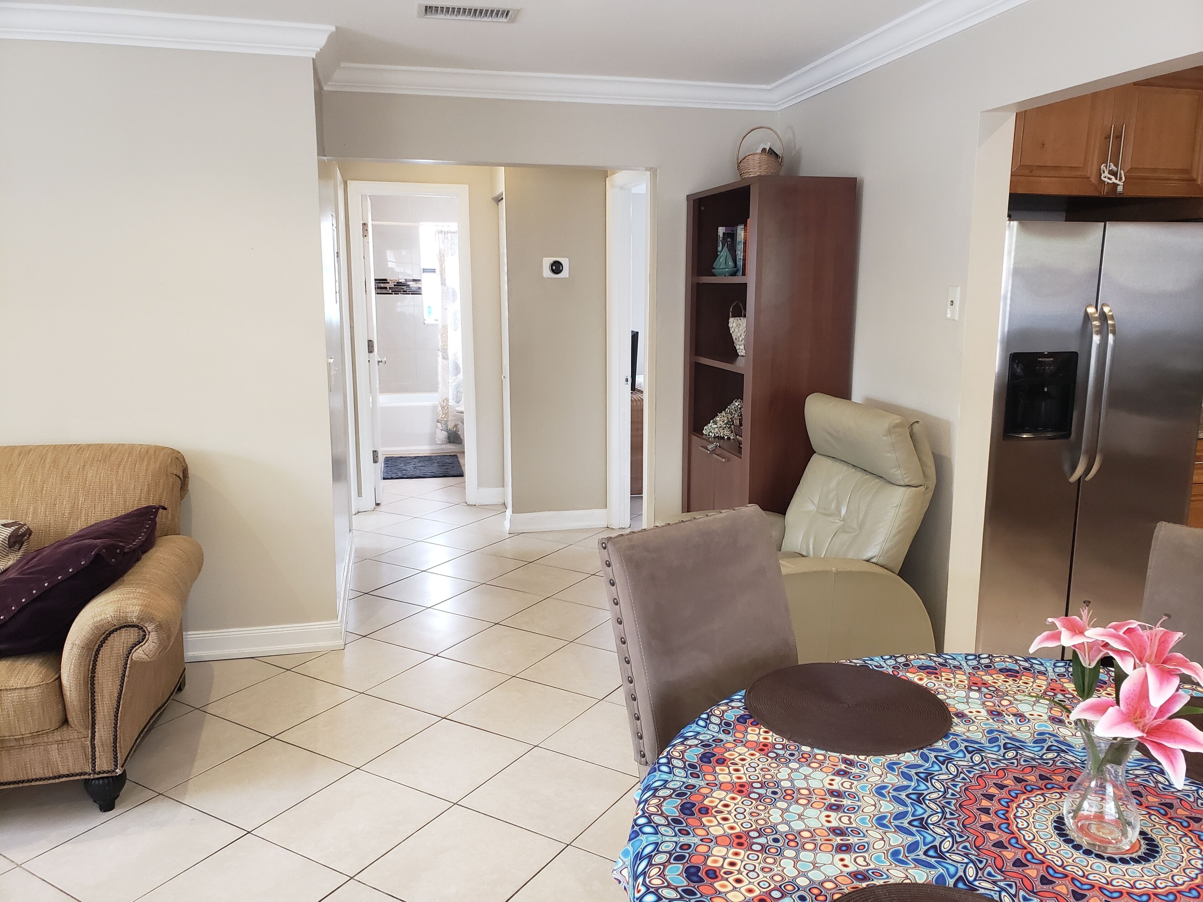 A living room with a beige sofa, a round coffee table with a colorful table runner, and a refrigerator in the background.