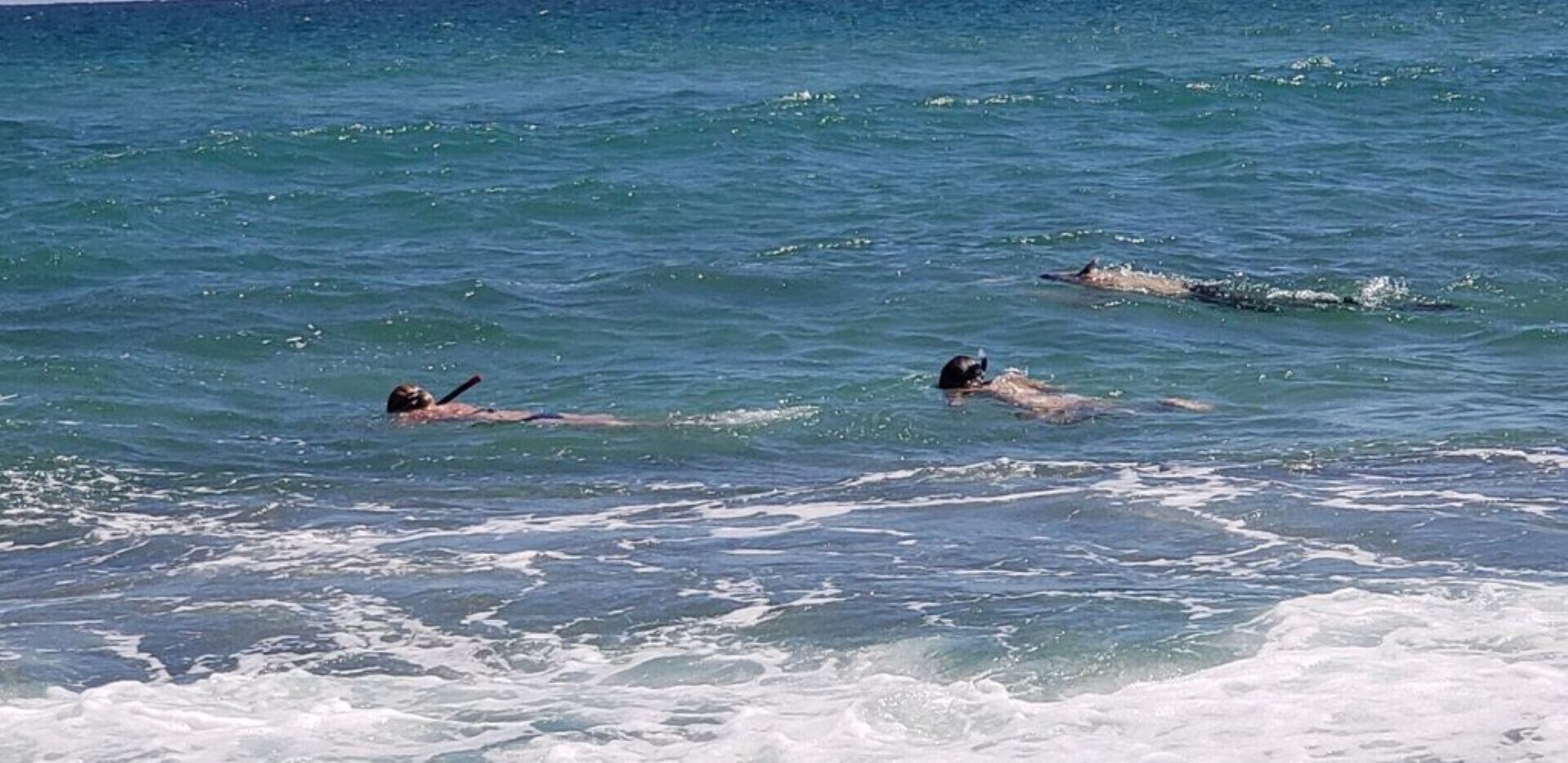 Une scène de plage où deux personnes nagent dans l’océan.