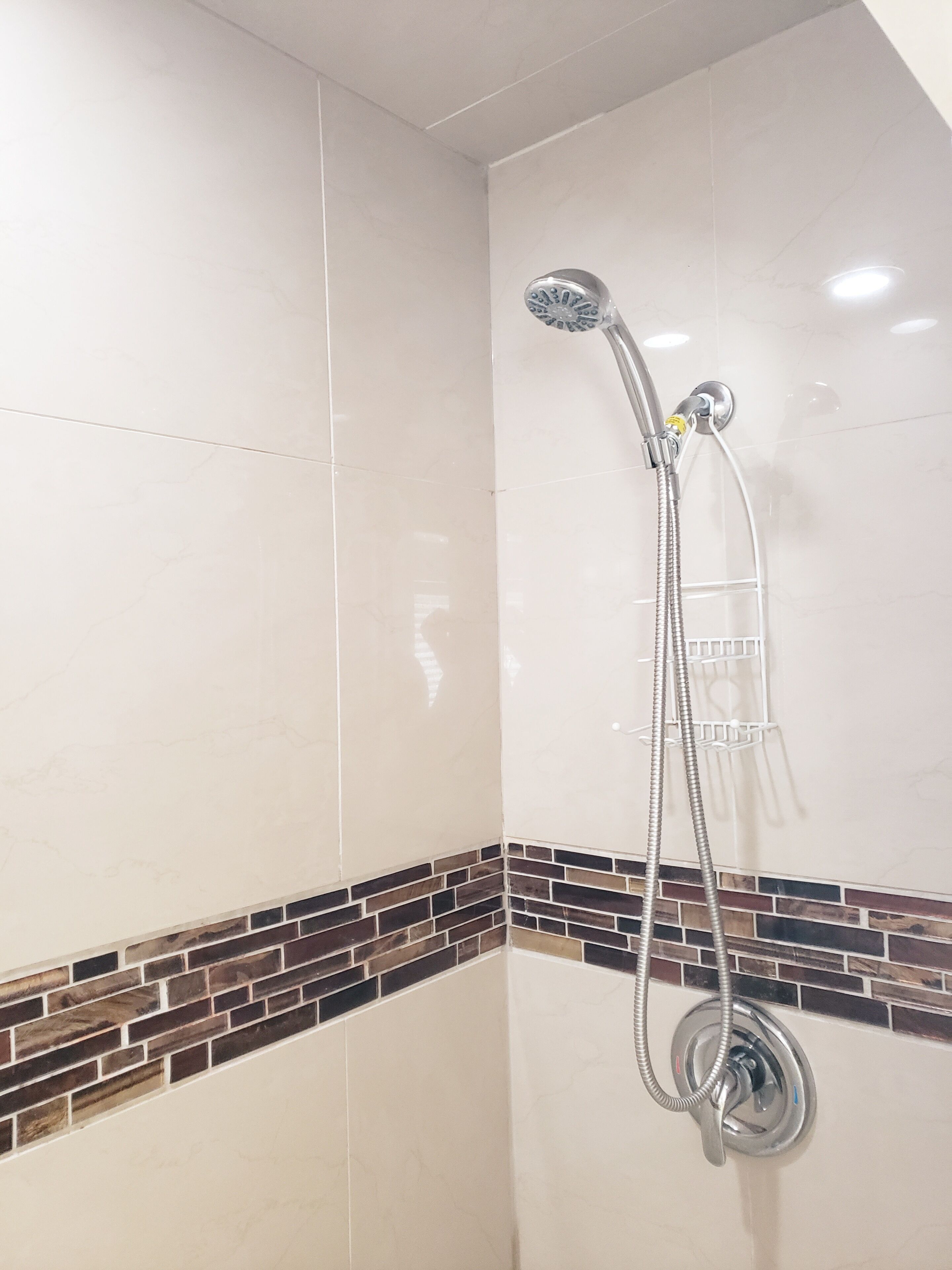 A shower with a handheld showerhead and a wall-mounted faucet.