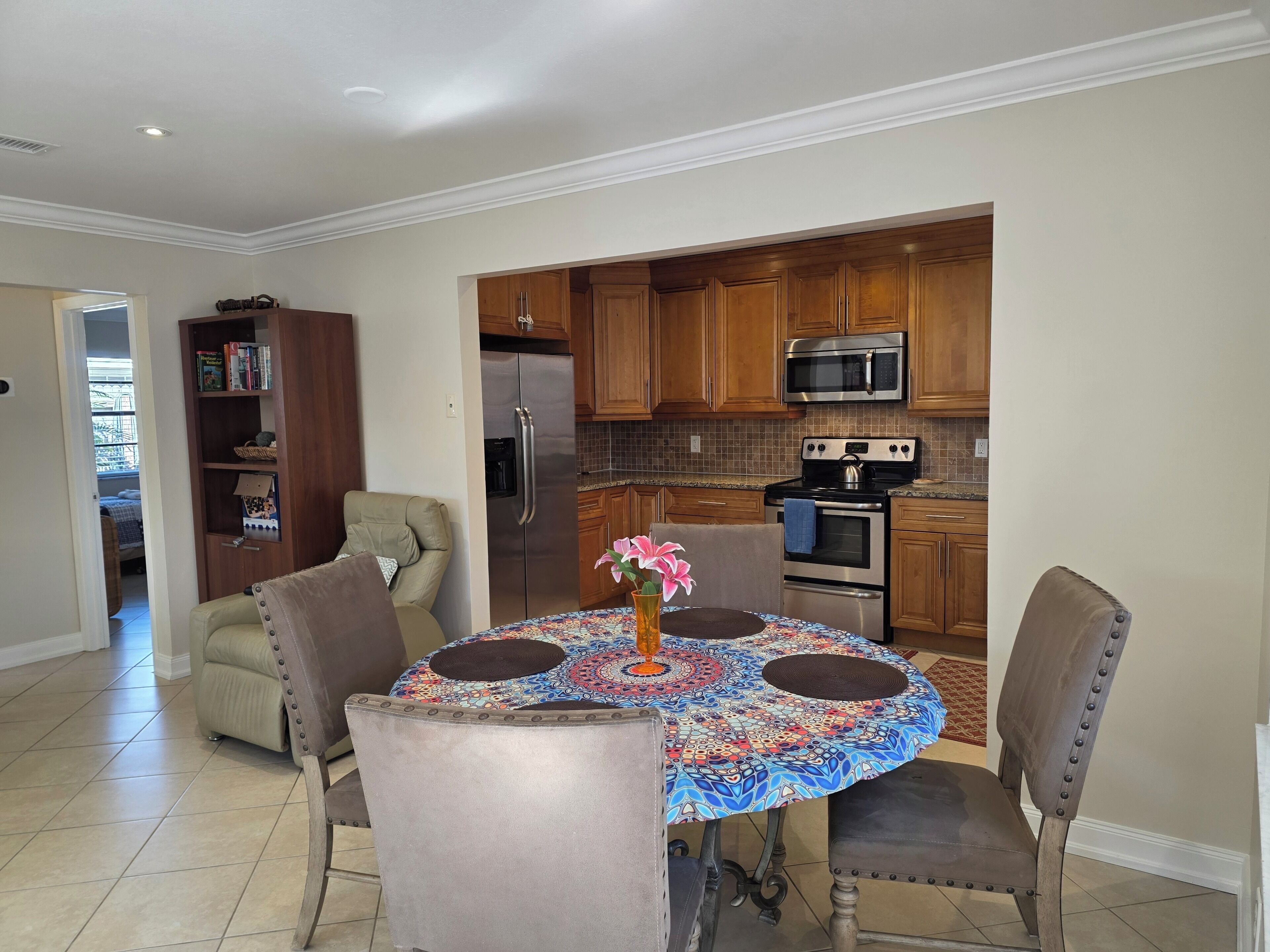 A dining area with a round table, four chairs, and a vase with flowers.