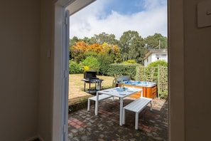 An outdoor patio area with a table and benches, a barbecue grill, and a hot tub. - Redwoods Haven - Spa Pool, Sleeps 9 (Rotorua)