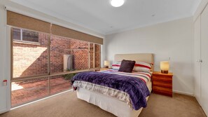 A bedroom with a large sliding glass door leading to a brick exterior, a bed with a striped bedspread, two bedside lamps, and a nightstand.