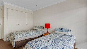A bedroom with two single beds, a wardrobe, and a red floor lamp. - Windarra on Denhams Unit Two (DENHAMS BEACH)